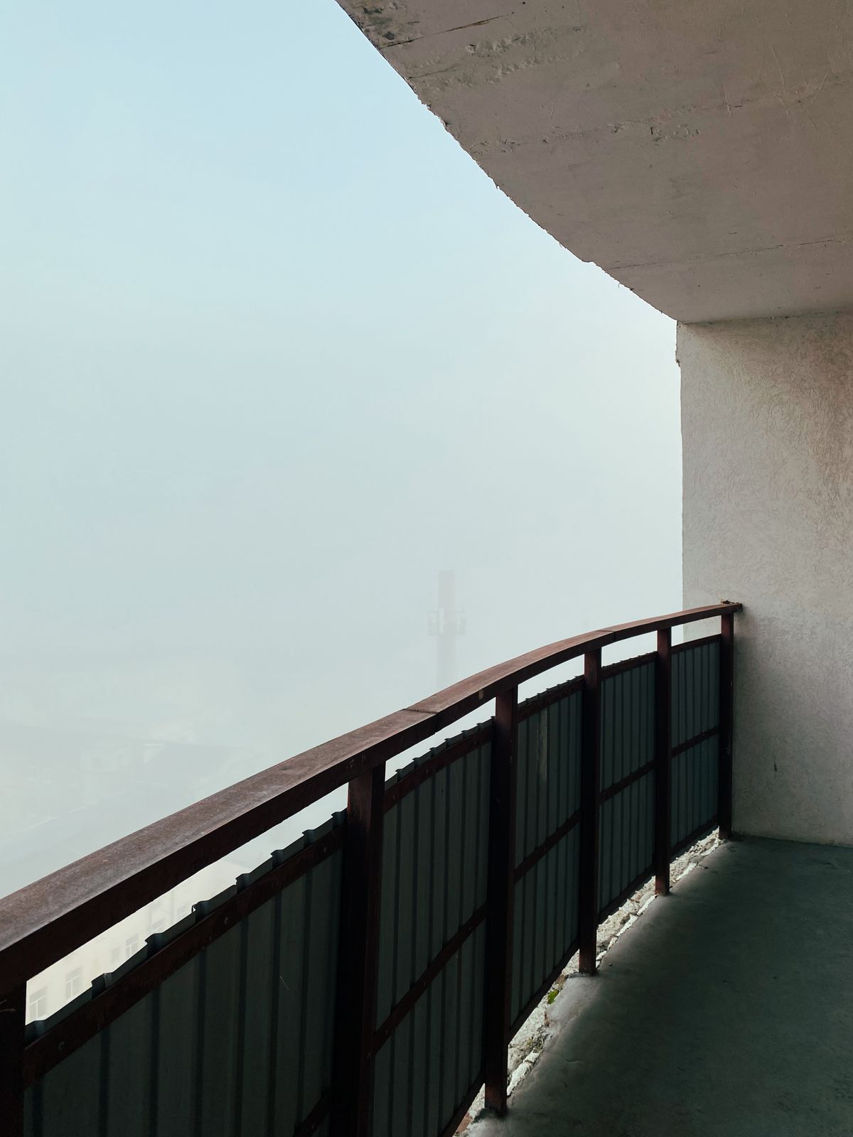 A misty, fog-obscured view from a building balcony, with the landscape beyond barely visible through the haze