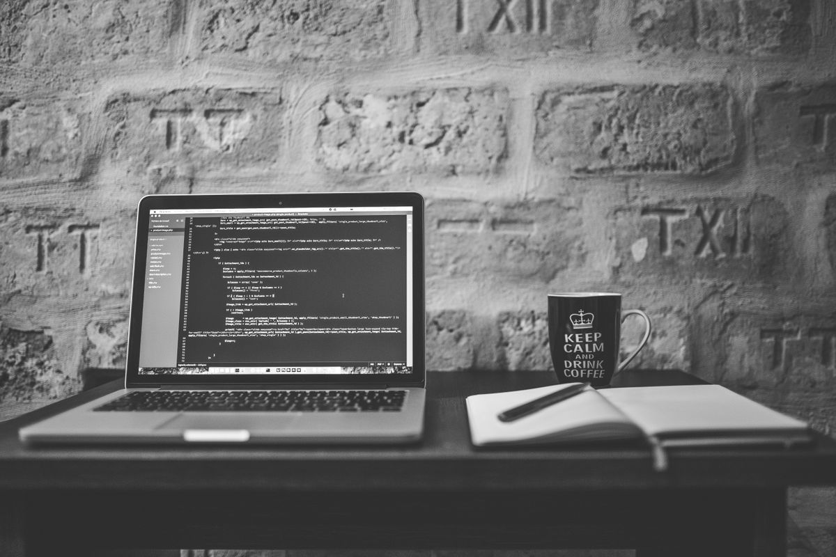 Black and white photo of a coding workspace with a laptop, mug, and notebook, representing how to add REST API legacy Java application development