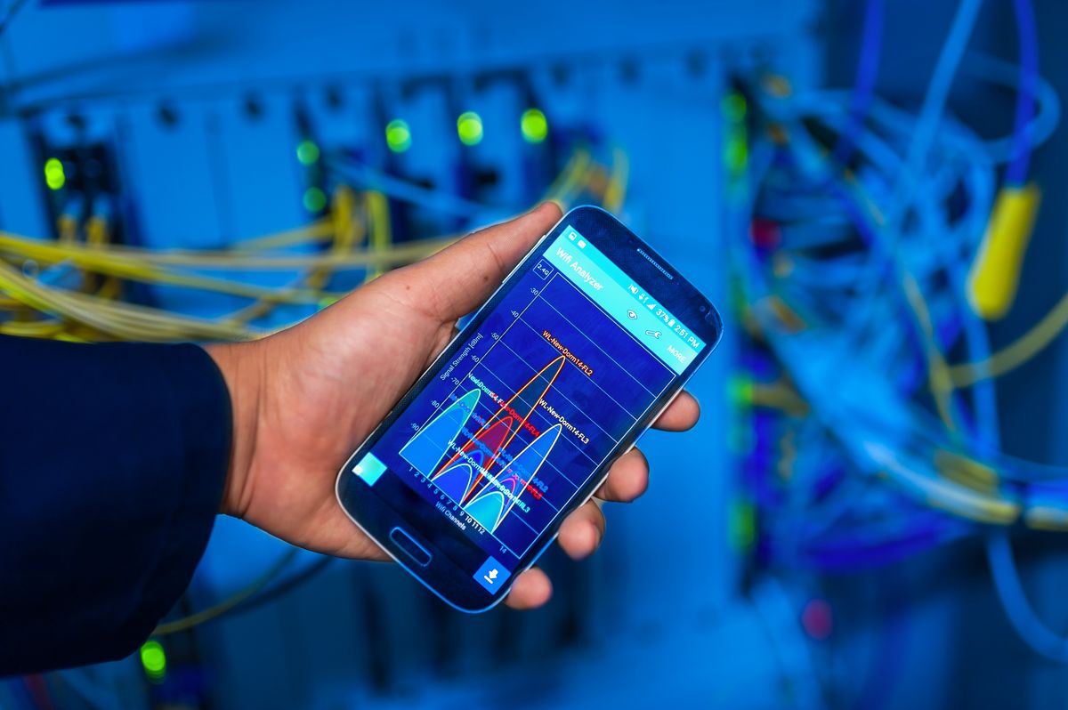 Hand holding smartphone displaying network analysis in high-tech server environment representing saas api load testing before launch and performance monitoring