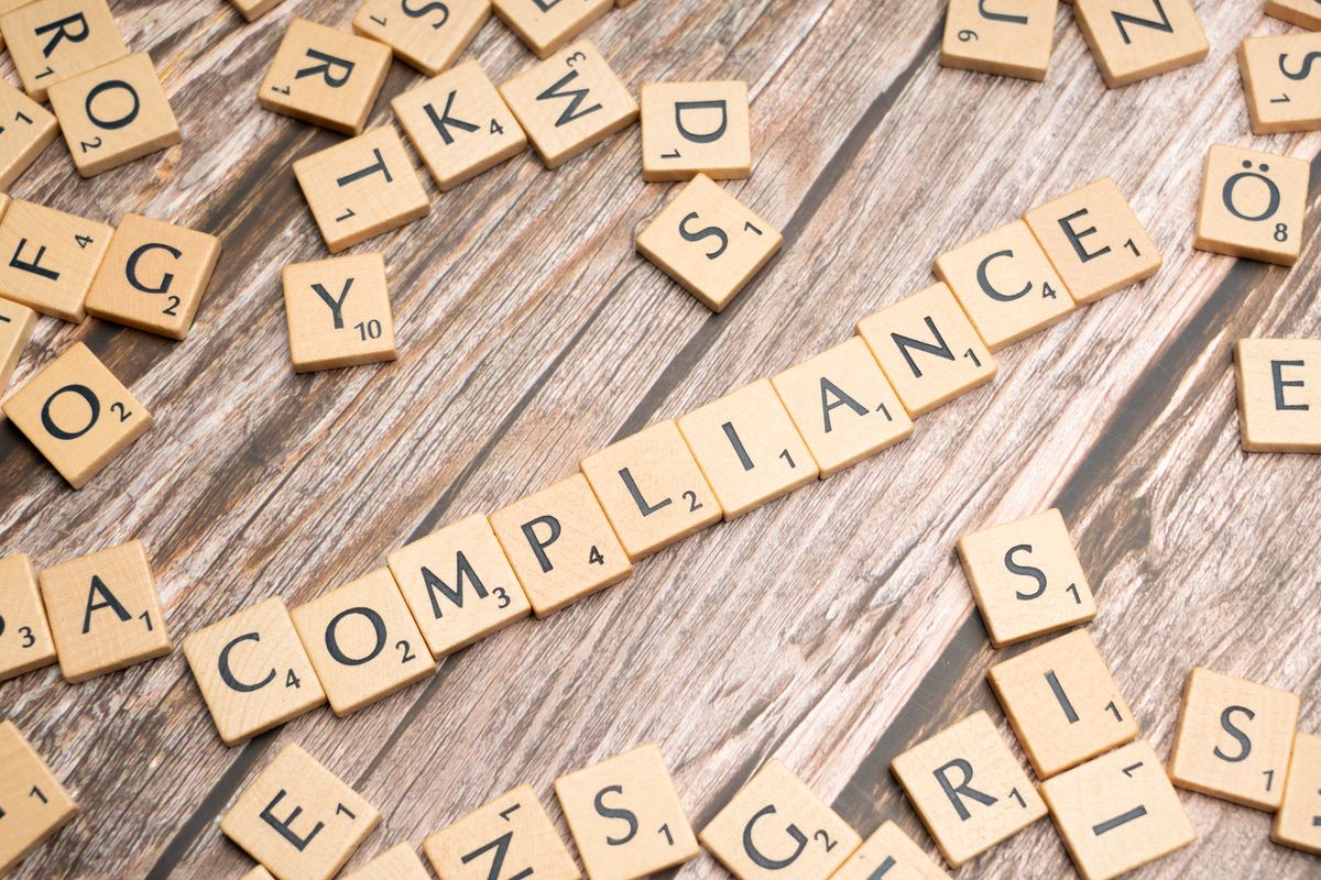 Wooden letter tiles spelling the word 'COMPLIANCE' on a rustic wooden background