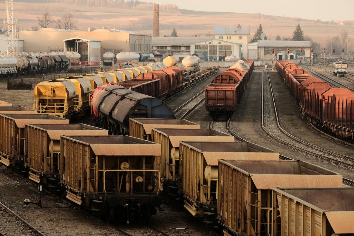 A busy freight train yard with rows of cargo cars on multiple tracks, representing a continuously running worker process compared to Lambda's short, disconnected bursts