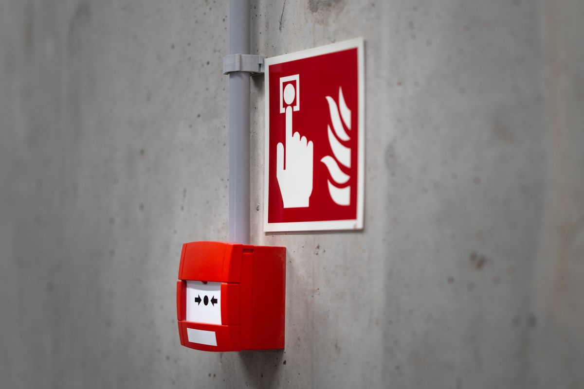 A red fire alarm button mounted on a concrete wall, representing the alert worth raising only once a Redis disruption genuinely exceeds the expected deploy window
