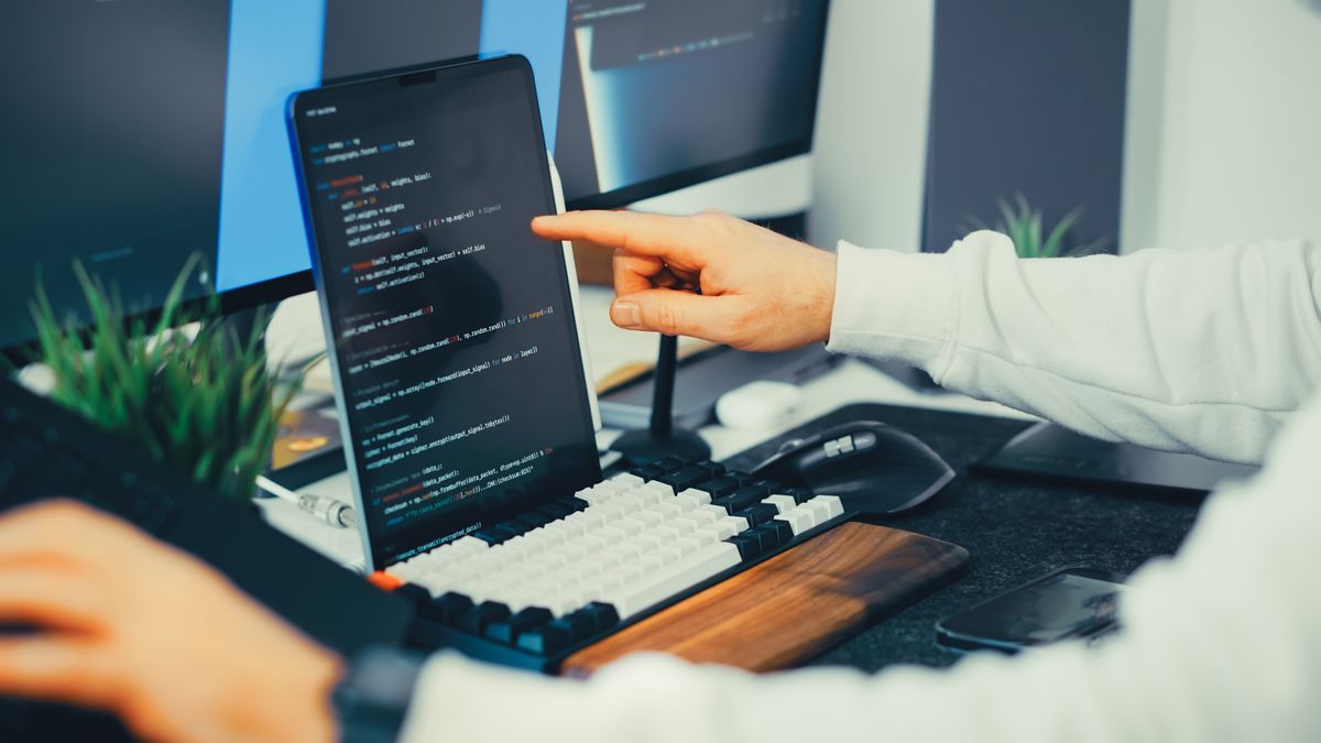 Web developer testing schema changes on a laptop and desktop setup in a modern workspace