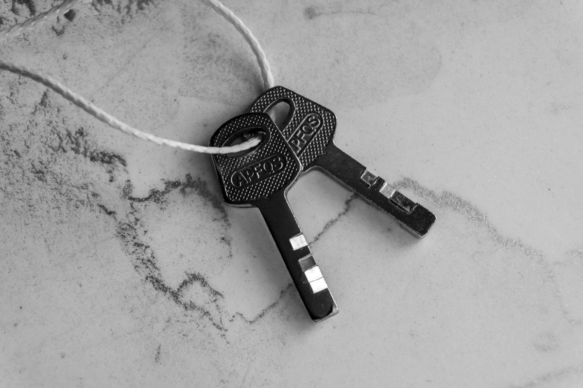 Two identical metal keys tied together with string on a marble surface, representing the duplicated internal connections BullMQ creates to support Redis's blocking commands