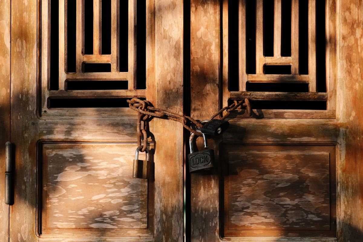 A rustic wooden door secured with a heavy chain and padlock, representing a database role denied the permission it needs to create anything