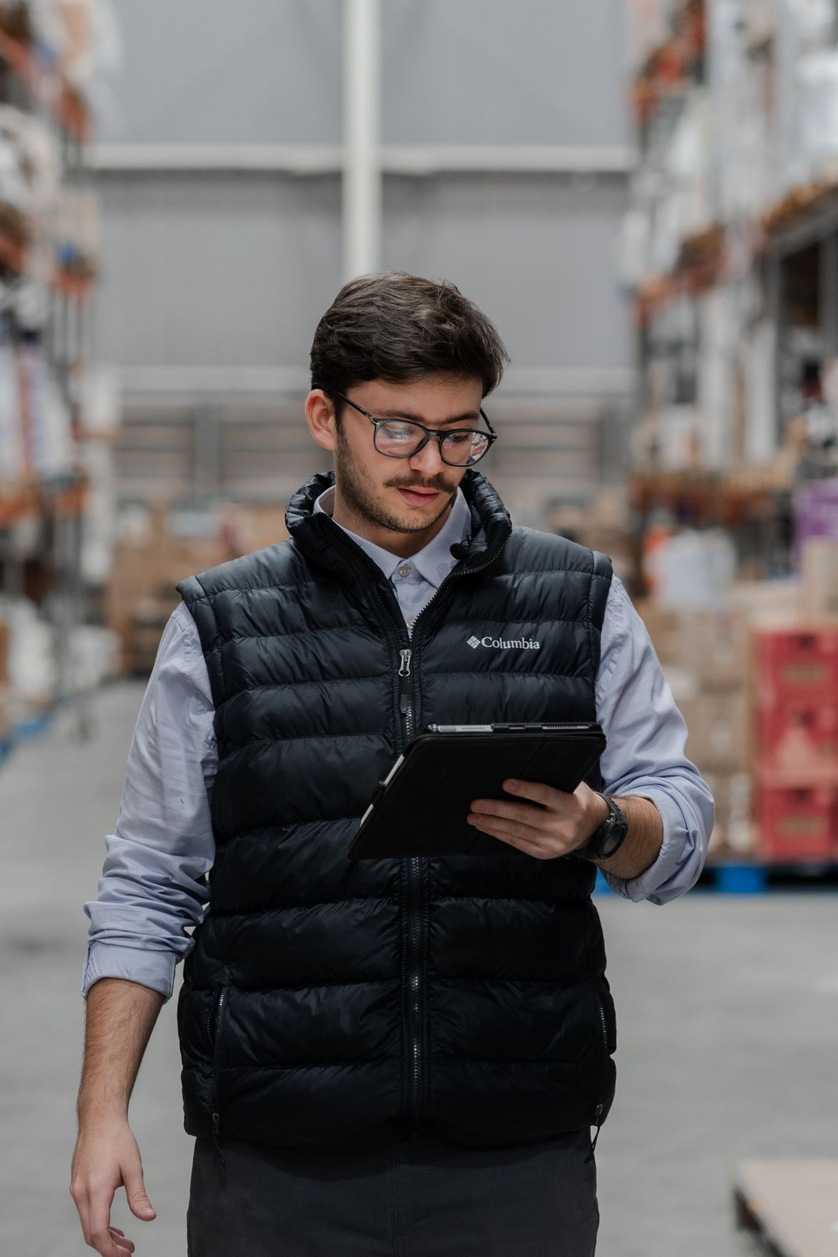 A warehouse worker checking inventory on a tablet surrounded by stacked boxes, representing the discipline of confirming every compiled file actually made it into the final Docker production stage