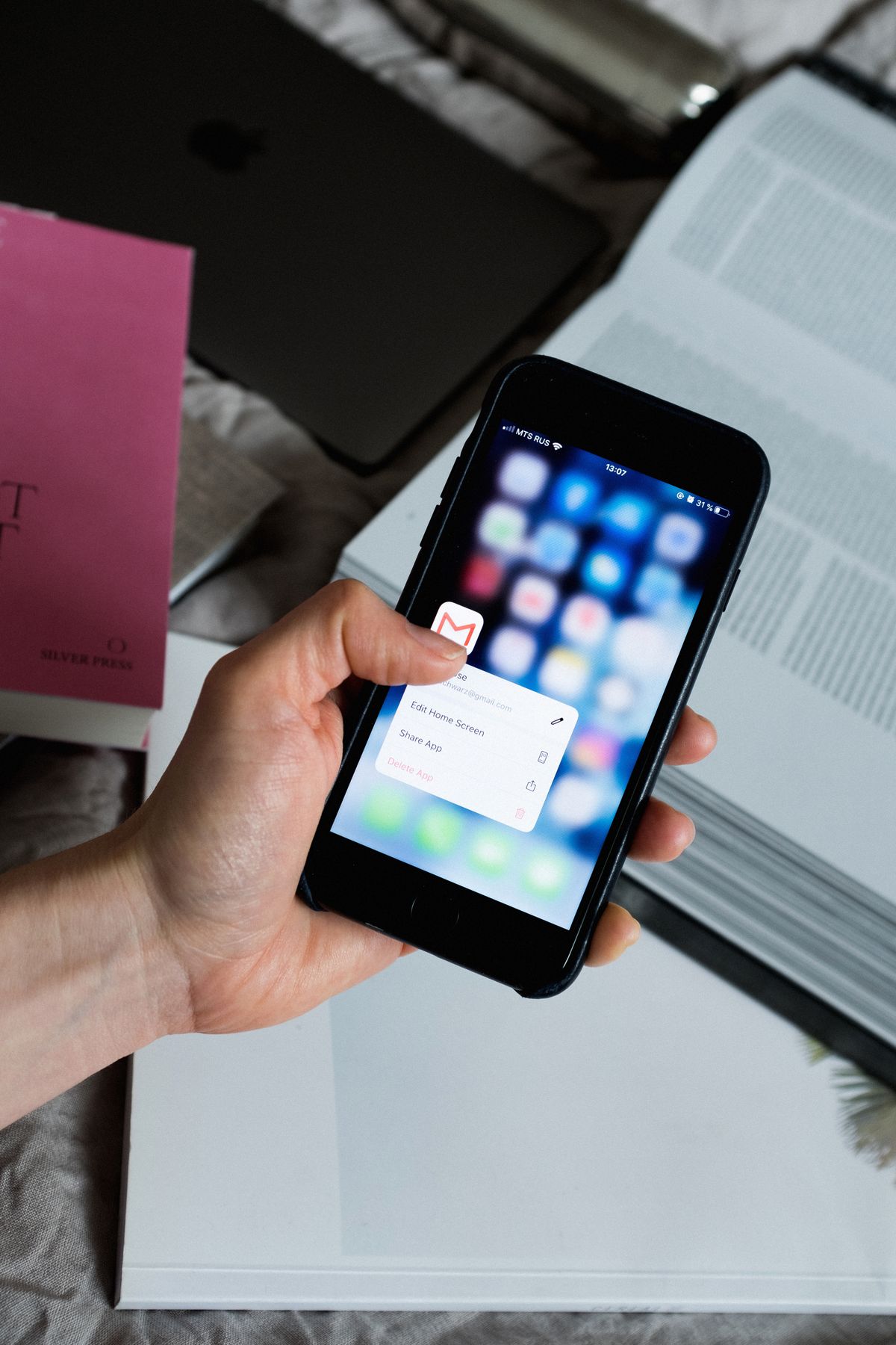 Hand holding a smartphone with an email app open, surrounded by a laptop and books