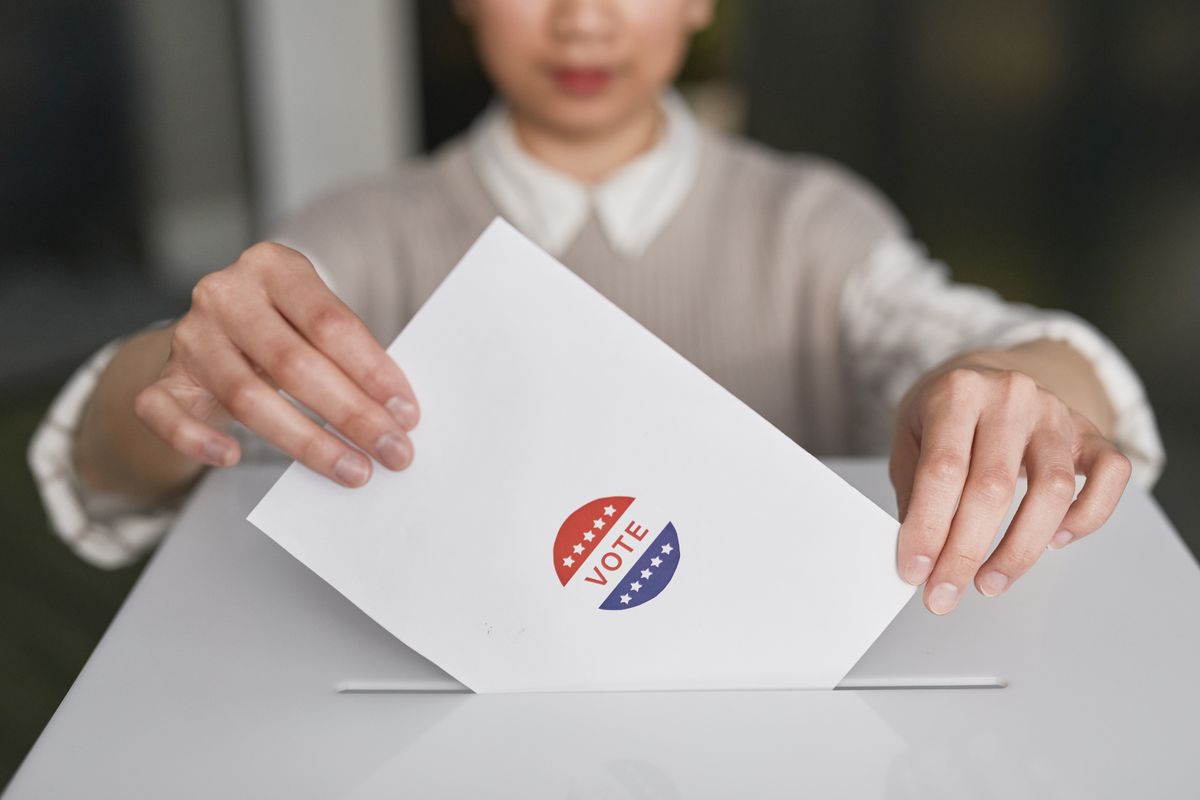 A person's hands placing a paper ballot marked with a 'VOTE' sticker into a ballot box slot, representing a form submission being sent directly to an external destination rather than processed by a server action