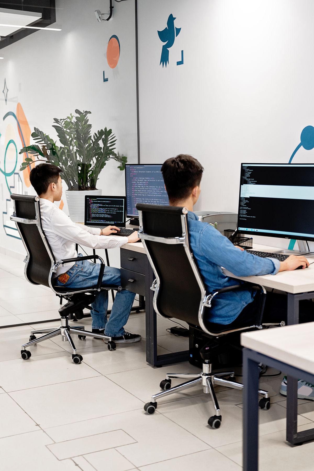 Two programmers collaborating in a bright, modern office, coding on monitors