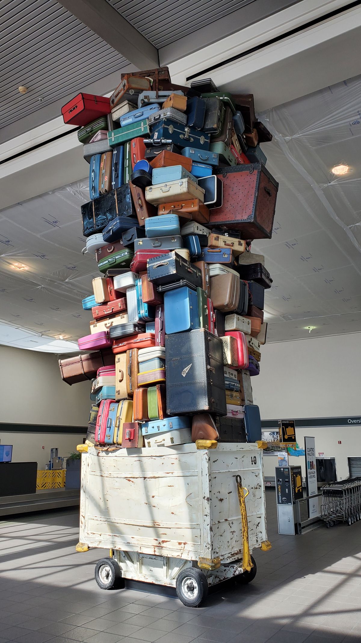 A large, disorganized pile of suitcases in an airport terminal, representing a deployment package bloated with binary targets the Lambda runtime never actually uses
